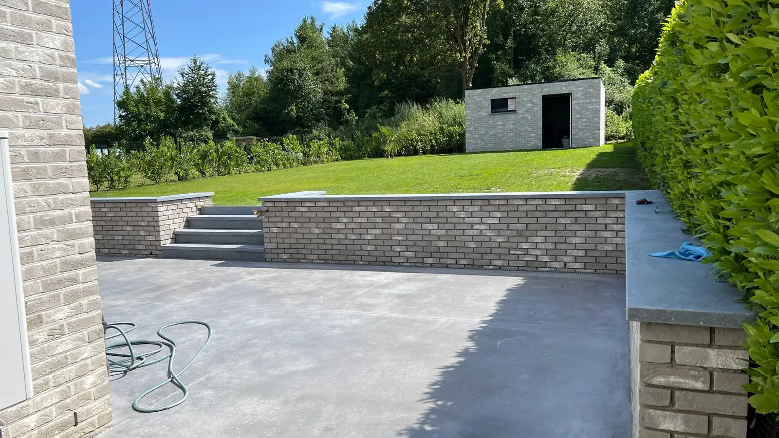 Terrasse en béton lissé bordée d'un muret en brique et d'un escalier