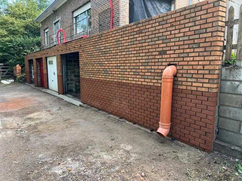 Mur de façade en brique reconstruit après rénovation, avec descente d'eau pluviale